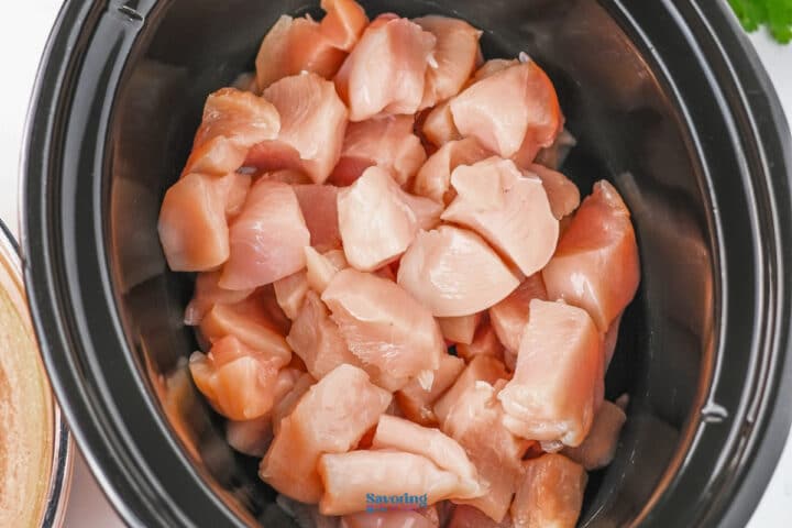 Chunks of raw chicken breast placed inside a black slow cooker.