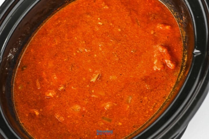 A slow cooker filled with hearty chicken tikka masala, featuring chunks of meat and vegetables simmered in a thick, spiced tomato-based sauce.
