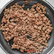 Cooked ground beef in a nonstick skillet on a stovetop, with some pieces browned and spread evenly across the pan.