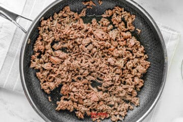 Cooked ground beef in a nonstick skillet on a stovetop, with some pieces browned and spread evenly across the pan.