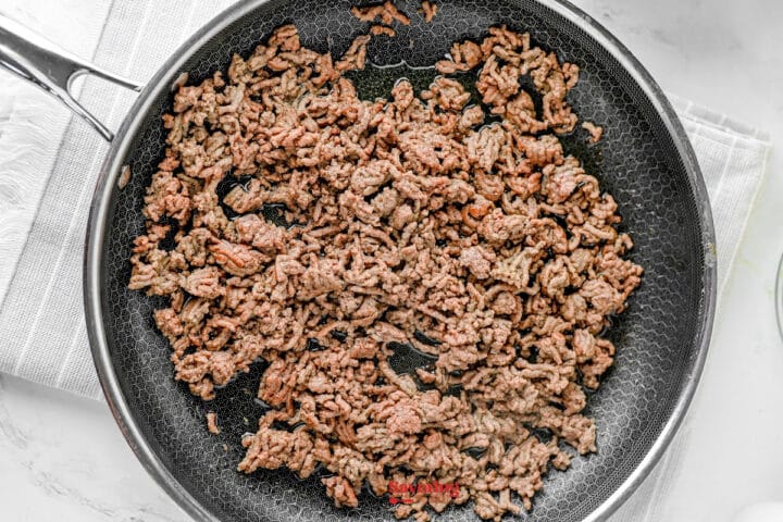 Cooked ground beef in a nonstick skillet on a stovetop, with some pieces browned and spread evenly across the pan.