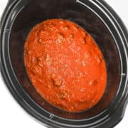 A slow cooker filled with rich red tomato sauce and ground meat, viewed from above-perfect for making a hearty lazy lasagna.
