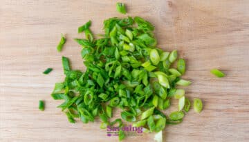 Chopped green onions scattered on a wooden cutting board.