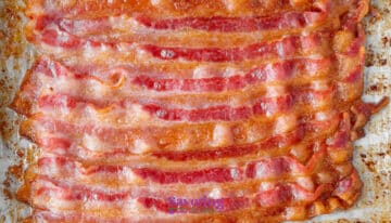 Several strips of cooked bacon are arranged side by side on a baking sheet lined with parchment paper.