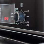 Close-up of a black oven control panel showing a temperature dial set around 200 degrees Celsius, digital display, and various function buttons.