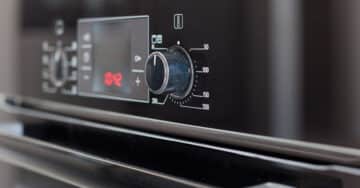 Close-up of a black oven control panel showing a temperature dial set around 200 degrees Celsius, digital display, and various function buttons.