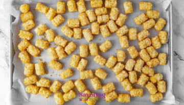 A baking sheet lined with parchment paper holds an even layer of frozen tater tots, ready to be baked.