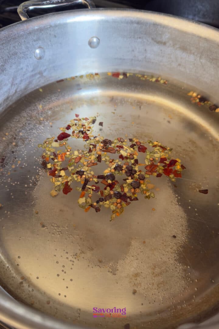 Stainless steel pan with oil heating and red pepper flakes scattered in the center.