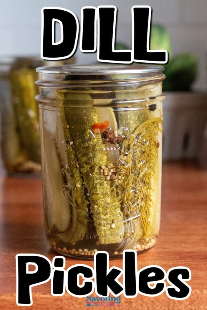A glass jar filled with dill pickles, herbs, and spices sits on a wooden surface. Bold text above and below reads “Dill Pickles.”.