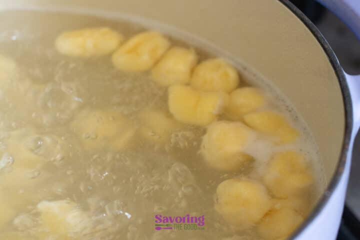 Yellow gnocchi pieces boiling in a pot of water, with bubbles rising to the surface.