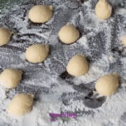 Small balls of dough are arranged on a floured dark surface, ready for baking or further preparation.