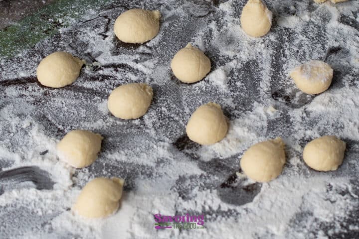Small balls of dough are arranged on a floured dark surface, ready for baking or further preparation.