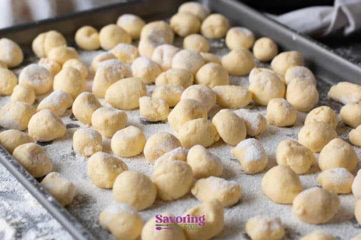 A baking sheet is covered with floured, uncooked gnocchi dough pieces, ready to be cooked.