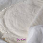A close-up of homemade ricotta cheese wrapped in a white cloth, partially uncovered, resting on a flat surface.