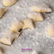 Uncooked gnocchi pieces dusted with flour are spread out on a floured surface, ready for cooking.