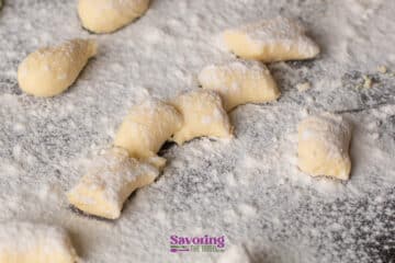 Uncooked gnocchi pieces dusted with flour are spread out on a floured surface, ready for cooking.