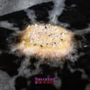 A breaded fried goat cheese is being deep fried in hot oil, with bubbles forming around it.