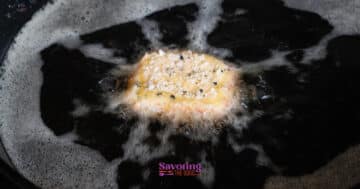 A breaded fried goat cheese is being deep fried in hot oil, with bubbles forming around it.