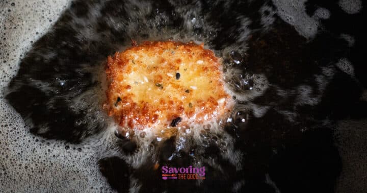 A golden hash brown patty is being deep fried in hot oil, with bubbles forming around its edges, much like a crisp disk of fried goat cheese sizzling to perfection.