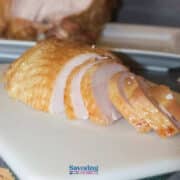 Sliced roasted turkey breast on a white cutting board, with a serving platter in the background.
