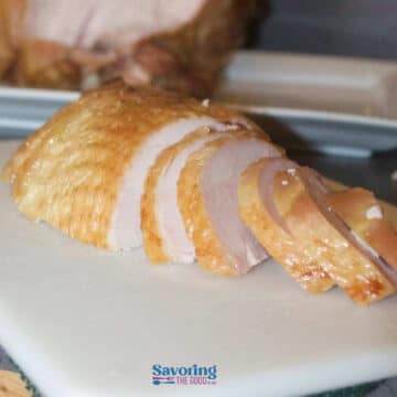 Sliced roasted turkey breast on a white cutting board, with a serving platter in the background.