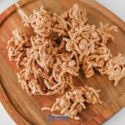 A pile of butterscotch haystack cookies made with chow mein noodles and butterscotch chips on a wooden platter.