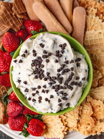 A bowl of cannoli dip topped with chocolate chips, surrounded by strawberries, ladyfingers, and waffle cookies.