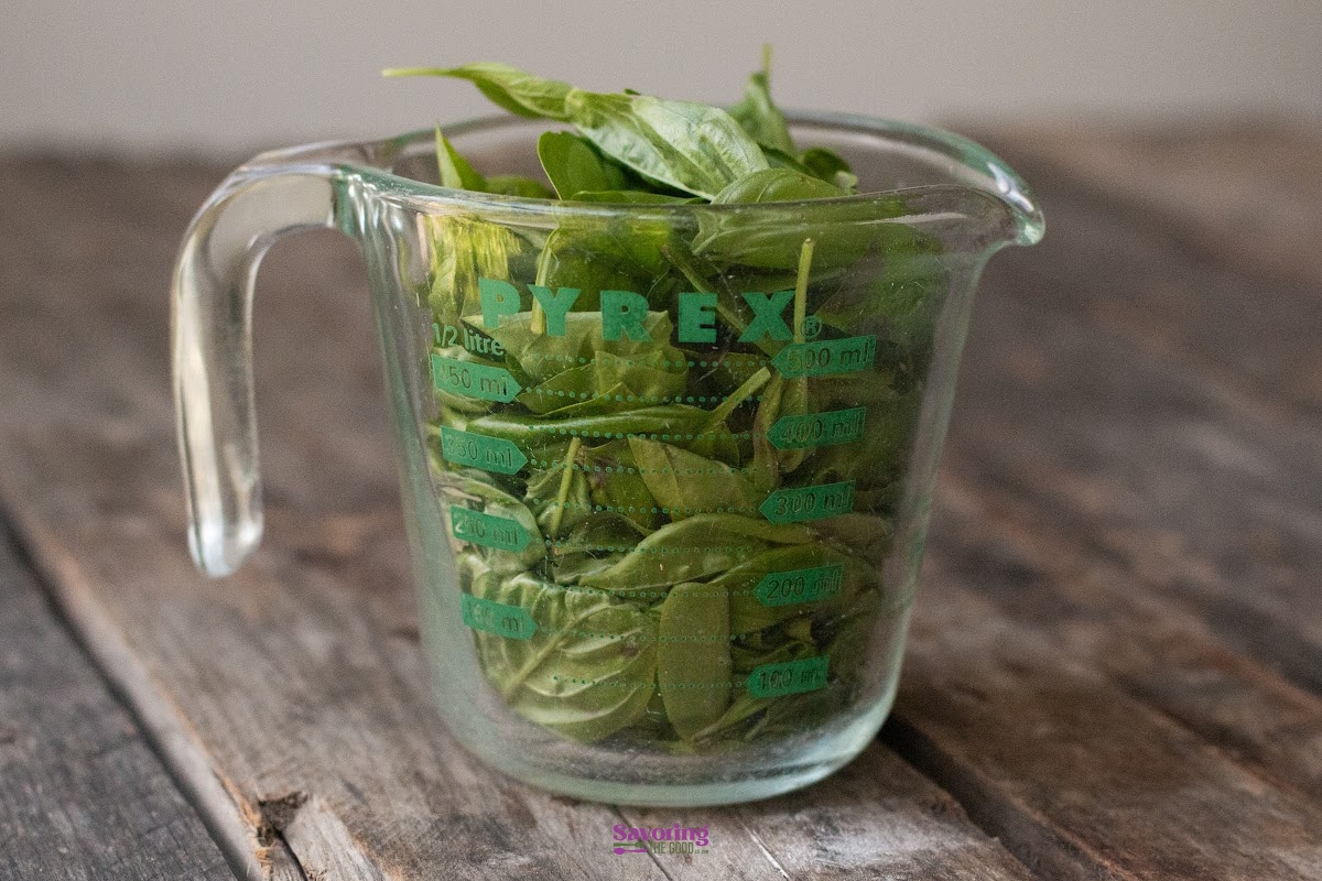 A glass measuring cup filled with fresh basil leaves.
