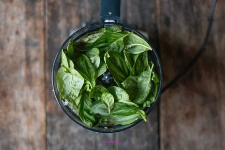 Fresh basil leaves inside a food processor bowl, viewed from above.