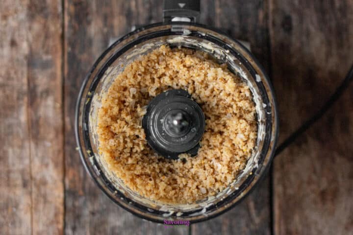 Food processor filled with finely chopped Parmesan cheese and nuts.