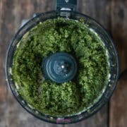 A food processor bowl filled with freshly processed green pesto.