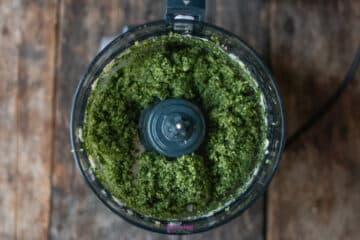 A food processor bowl filled with freshly processed green pesto.