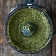 Green pesto in a food processor bowl, viewed from above.