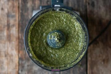 Green pesto in a food processor bowl, viewed from above.