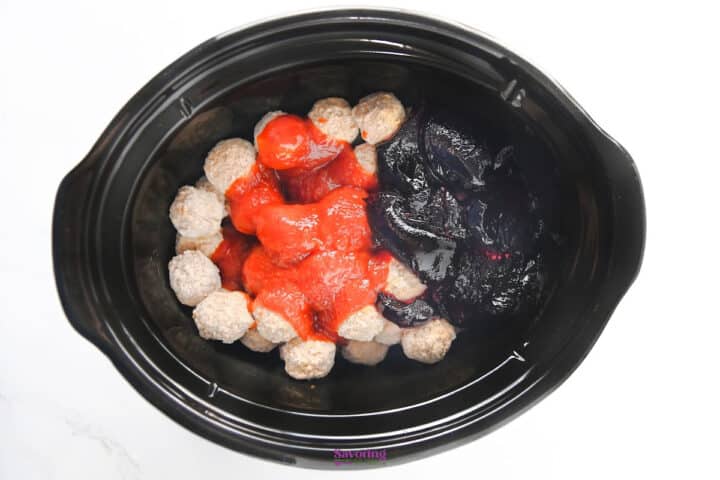 Meatballs in red sauce and dark grape jelly in a slow cooker insert.